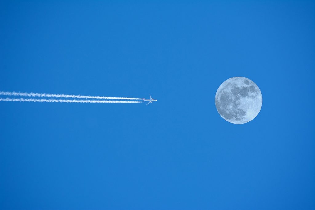A commercial airplane approching the full moon in a clear blue sky. High Flyer, moon, horizontal, copy space, Canada, outdoors shoot